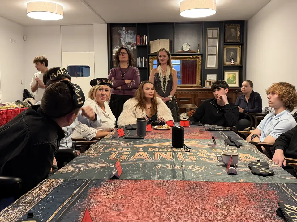 A long game table with red name cards and club guests in the room